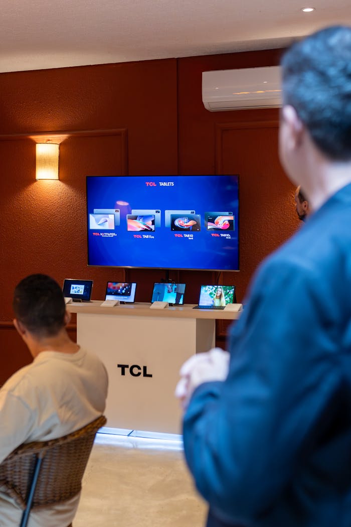 TCL products on display in a showroom, featuring tablets and monitors with people observing.